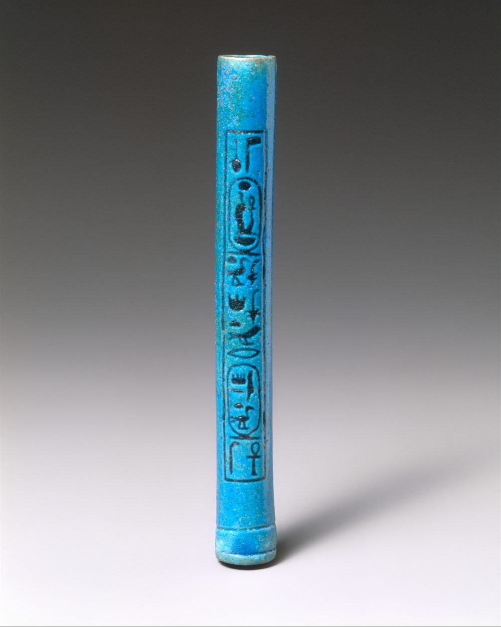 An upright turquoise-blue cylindrical tube with a column of black hieroglyphs, on a grey background.