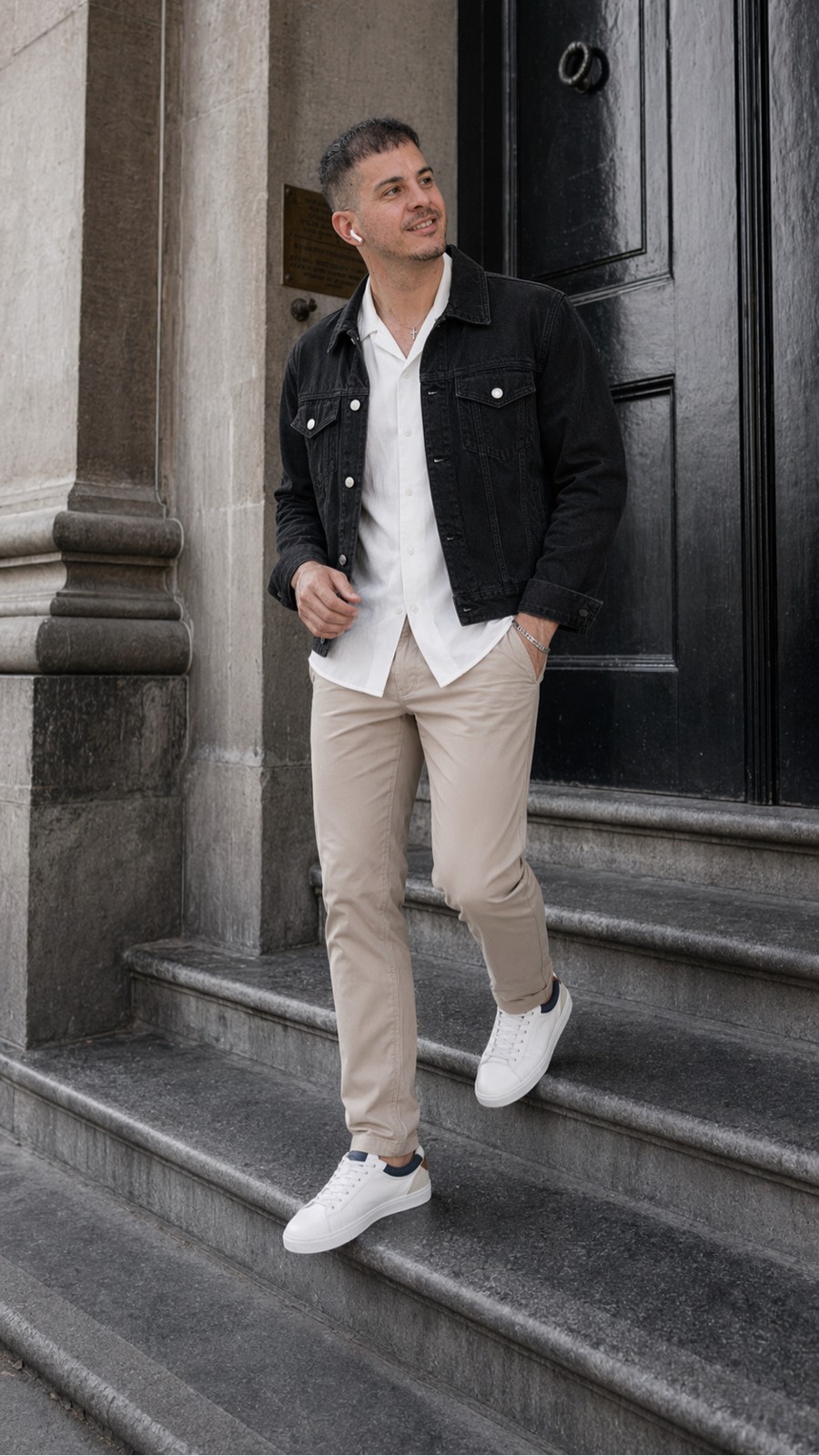 Chaqueta denim negra estilo trucker, camisa blanca relajada, chino beige y sneakers blancas con detalles navy: un look casual elegante, limpio y urbano.